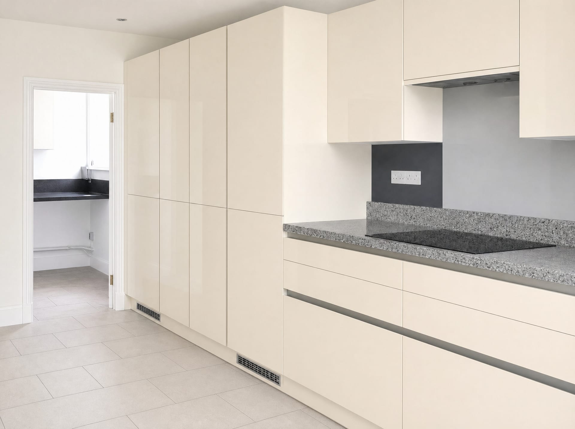 Handleless cream high-gloss kitchen with dark stone worktop and induction hob