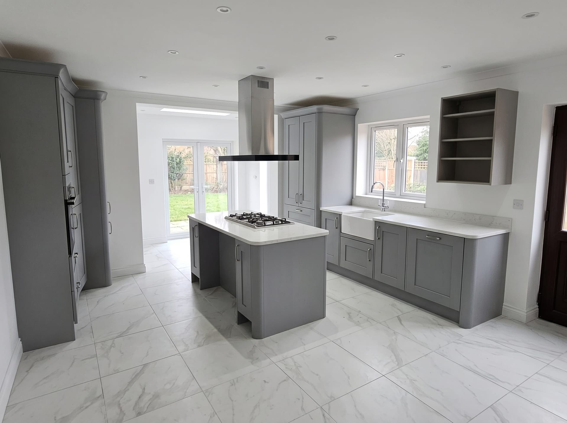 Open-plan grey shaker kitchen with central island, gas hob, Belfast sink and French doors to garden